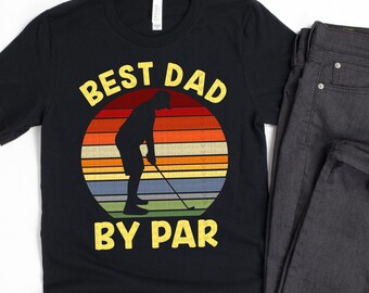 May include: Black t-shirt with a retro sunset graphic and a silhouette of a golfer. The text "Best Dad By Par" is printed in yellow.