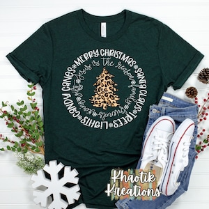 May include: A green t-shirt with a white circle design featuring a leopard print Christmas tree and the text "TREES LIGHTS CANDY CANES * MERRY CHRISTMAS * Jesus is the reason * family * Friendsgiving * SANTA CLAUS".