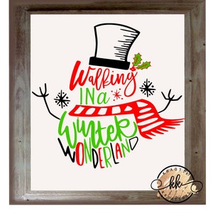 Puede incluir: Un letrero enmarcado con un diseño de muñeco de nieve. El muñeco de nieve lleva un sombrero de copa negro y una bufanda roja. El texto "Walking in a Winter Wonderland" está escrito en rojo y verde. El marco es de color marrón claro.