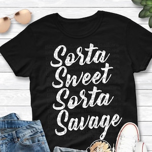 Pode incluir: Camiseta preta com texto branco que diz "Sorta Sweet Sorta Savage". A camiseta &eacute; mostrada em uma modelo que usa jeans azul e t&ecirc;nis branco.