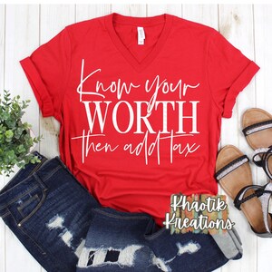 May include: A red V-neck t-shirt with the text "Know your WORTH then add Tax" in white script. The shirt is paired with distressed blue jeans and black and silver sandals. A small plant is also in the image.
