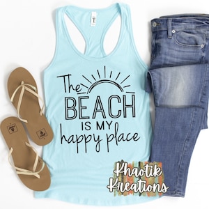 May include: A light blue tank top with the text "The Beach is my happy place" in black. A sun graphic is above the text. The tank top is on a white background with a pair of brown flip flops and blue jeans.