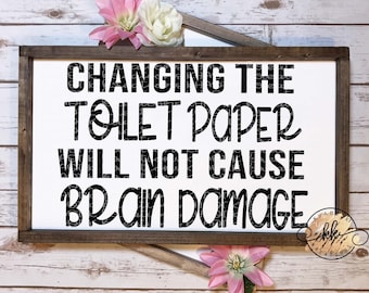May include: A white wooden sign with black text that reads "Changing the toilet paper will not cause brain damage". The sign is surrounded by pink flowers.
