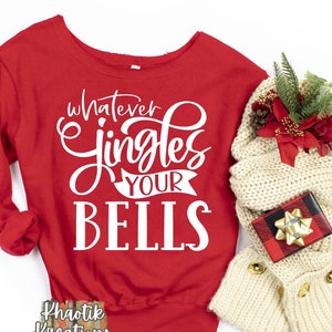 Puede incluir: Una sudadera roja de manga larga con la frase "whatever jingles your bells" en escritura blanca. Una bufanda color crema, una pequeña caja de regalo y vegetación decorativa están junto a la sudadera. Es un artículo festivo.