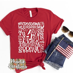 May include: A red t-shirt with a white graphic design featuring the text "Freedom," "4th of July," and "Home of the Brave." The design includes stars, stripes, and fireworks. Sunglasses, denim shorts, and a small American flag are also visible.