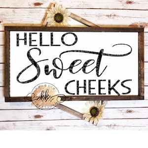 May include: A wooden sign with the text "Hello Sweet Cheeks" in black script font. The sign is on a white wood background with sunflowers.
