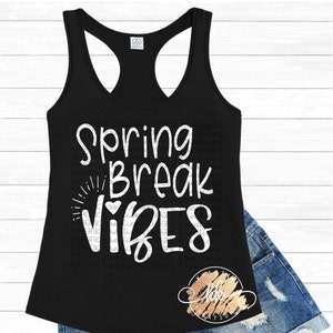 May include: Black tank top with white text that reads "Spring Break Vibes" with a heart symbol. The tank top is laying on a pair of blue denim shorts.