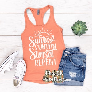 May include: A coral orange tank top with the text "Sunrise Suntan Sunset Repeat" in white. The text is in a handwritten style font. The tank top is laying on a white wooden surface with a pair of white sneakers and a pair of blue denim shorts. The text "Khaotik Kreations" is in the bottom right corner of the image.