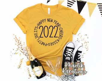 May include: A mustard yellow t-shirt with a black circle graphic that says "Party Like It's Happy New Year 2022 Kisses Cheers".