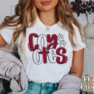 May include: White t-shirt with a red and white graphic that says "Coyotes" with paw prints.