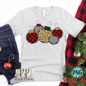 May include: A gray t-shirt with a design of five Christmas ornaments. The ornaments are red and black plaid, black and white houndstooth, and leopard print.