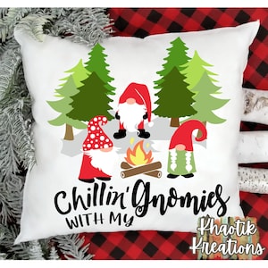 May include: White throw pillow with a design of three gnomes sitting around a campfire in a forest. The text "Chillin' with my Gnomies" is written below the gnomes. The text "Khaotik Kreations" is written in the bottom right corner.