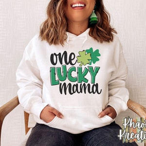 K&ouml;nnte beinhalten: Wei&szlig;er Hoodie mit einem gr&uuml;nen Kleeblatt und dem Text "one lucky mama" auf der Vorderseite.