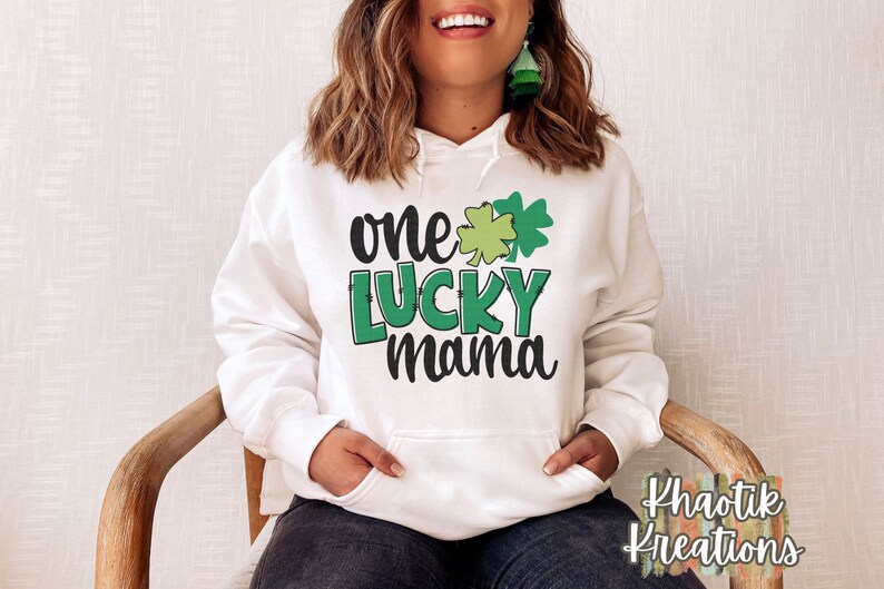 K&ouml;nnte beinhalten: Wei&szlig;er Hoodie mit einem gr&uuml;nen Kleeblatt und dem Text "one lucky mama" auf der Vorderseite.