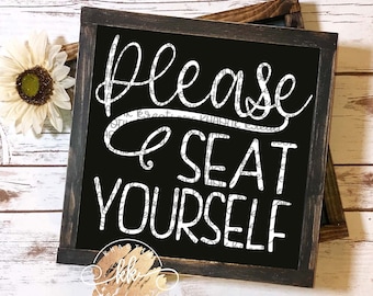 May include: A black chalkboard sign with white text that reads "Please be seat yourself". The sign is framed in a dark wood frame.
