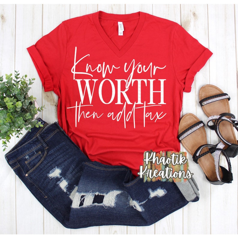 May include: A red V-neck t-shirt with the text "Know your WORTH then add Tax" in white script. The shirt is paired with distressed blue jeans and black and silver sandals. A small plant is also in the image.