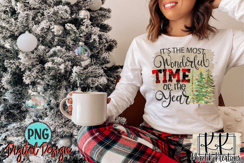 May include: A white long-sleeved shirt with the text "It's the most Wonderful Time of the Year" in black script with a red and black plaid pattern behind the word "Time". The shirt is decorated with a green Christmas tree with red and white baubles and lights.
