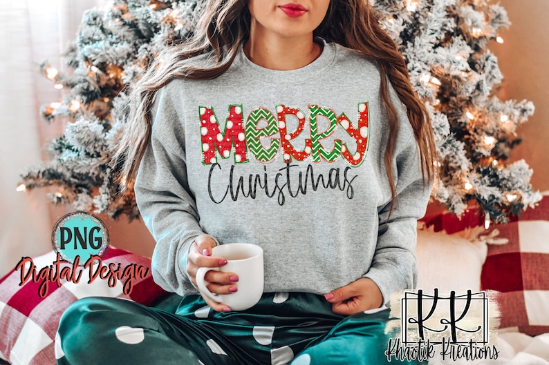 May include: A gray sweatshirt with the words "Merry Christmas" in red, green, and white patterned letters. The letters are decorated with polka dots, zigzags, and snowflakes.