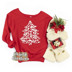 May include: Red sweatshirt featuring a white leopard print Christmas tree design. The text "Khaotik Kreations" is printed on the bottom of the sweatshirt.