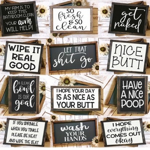 May include: Collection of framed bathroom signs with humorous phrases in white script on black or white backgrounds. Phrases include "My aim is to keep this bathroom clean", "So fresh & so clean", and "Nice Butt".