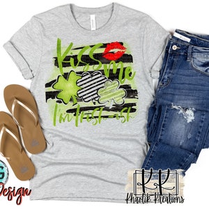 May include: A gray t-shirt with a black and white striped design and green shamrocks. The text "Kiss me I'm Irish-ish" is written in green. A red lip print is above the text.