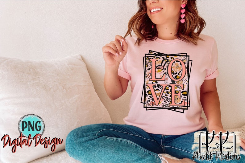 Pu&ograve; includere: Una maglietta rosa con un design grafico della parola "LOVE" in lettere rosa circondata da una cornice nera e motivi floreali e animalier.