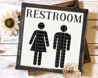 Può includere: Un cartello bianco e nero con la parola "RESTROOM" in grandi lettere. Il cartello ha una cornice in legno rustica e presenta un simbolo di toilette per uomini e donne. I simboli sono riempiti con il testo "KHAOTIK KREATIONS" ripetuto più volte.