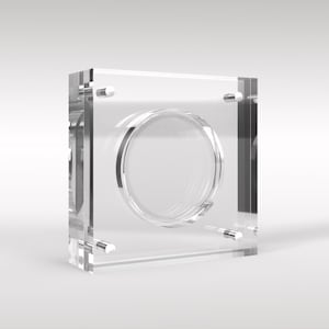 May include: A clear acrylic coin display case with a circular cutout in the centre. The case has four small metal posts on the sides.