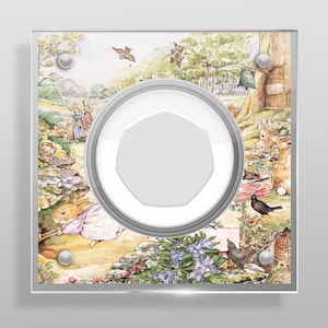 May include: A clear acrylic frame with a white background and a circular cutout. The frame features a colorful illustration of Peter Rabbit and his friends in a woodland setting. The illustration includes a variety of animals, flowers, and trees.
