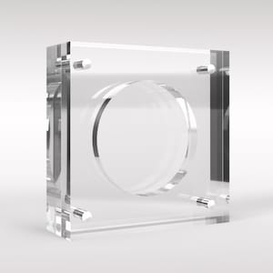 Peut inclure: Une vitrine de présentation de pièces de monnaie en acrylique transparent avec une ouverture circulaire au centre. La vitrine est dotée de quatre petits poteaux métalliques sur les côtés.