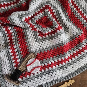 May include: A square crochet blanket featuring a concentric square pattern in red, white, and gray yarn. An appliqued brown baseball bat with a black handle and a white baseball with red stitching are attached to the corner. A small tag reads southerncraftgifts.