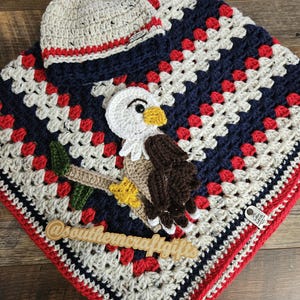 May include: A crocheted baby blanket and hat set in red, white, and navy blue. The blanket features a granny square design with a crocheted eagle applique. The hat has a red and white striped brim. The blanket and hat are handmade.