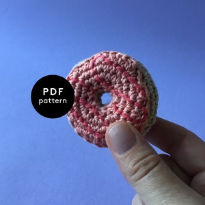 Könnte beinhalten: Ein gehäkelter Donut in Rosa und Grün mit einem Loch in der Mitte. PDF-Muster.