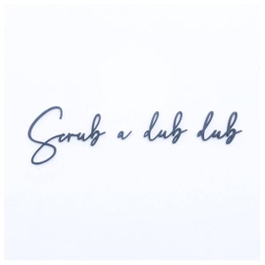 May include: Black cursive script lettering on a white background that reads "Scrub a dub dub".