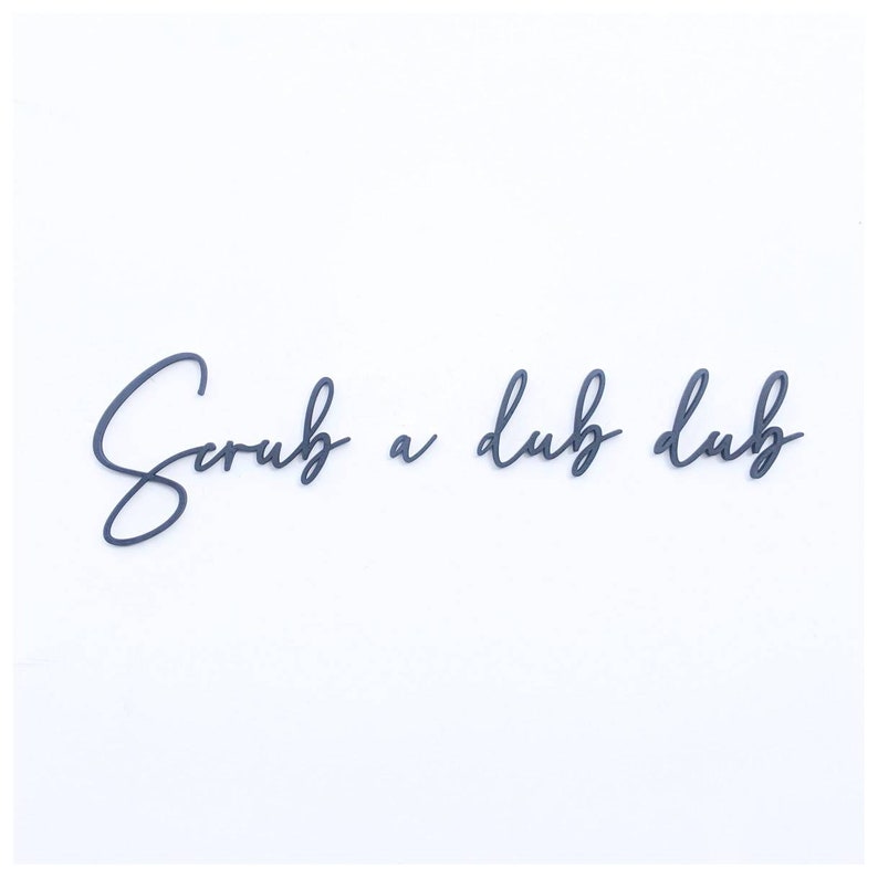 May include: Black cursive script lettering on a white background that reads "Scrub a dub dub".