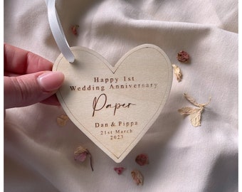 May include: A wooden heart-shaped ornament with the text "Happy 1st Wedding Anniversary Paper Dan & Pippa 21st March 2023" engraved on it.