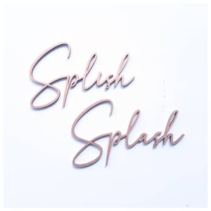 May include: Two wooden signs with the words "Splish" and "Splash" written in a cursive script. The signs are painted in a rose gold color.