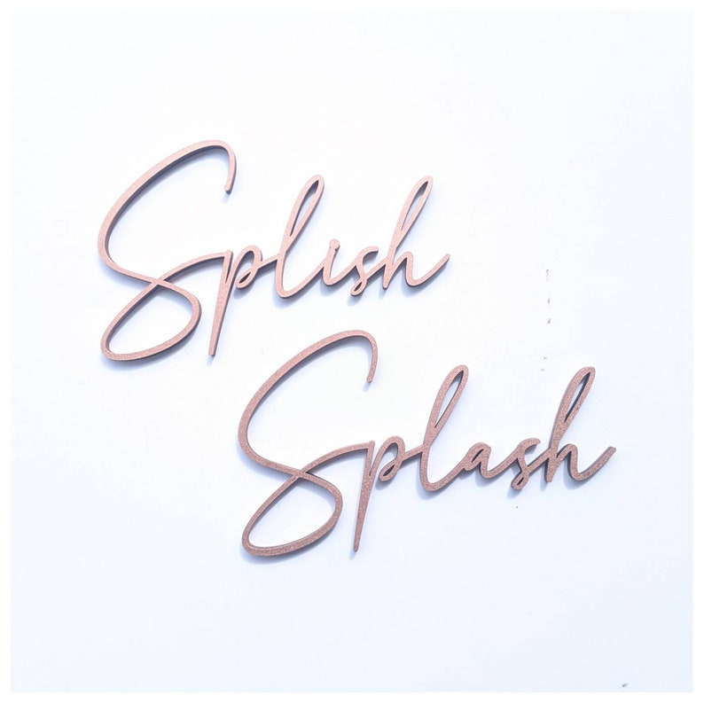 May include: Two wooden signs with the words "Splish" and "Splash" written in a cursive script. The signs are painted in a rose gold color.