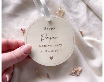 May include: A round wooden ornament with the text "Happy Paper Anniversary 1st March 2023" and a small heart.