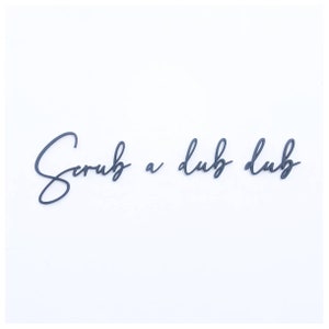 May include: Black cursive script lettering on a white background that reads "Scrub a dub dub".