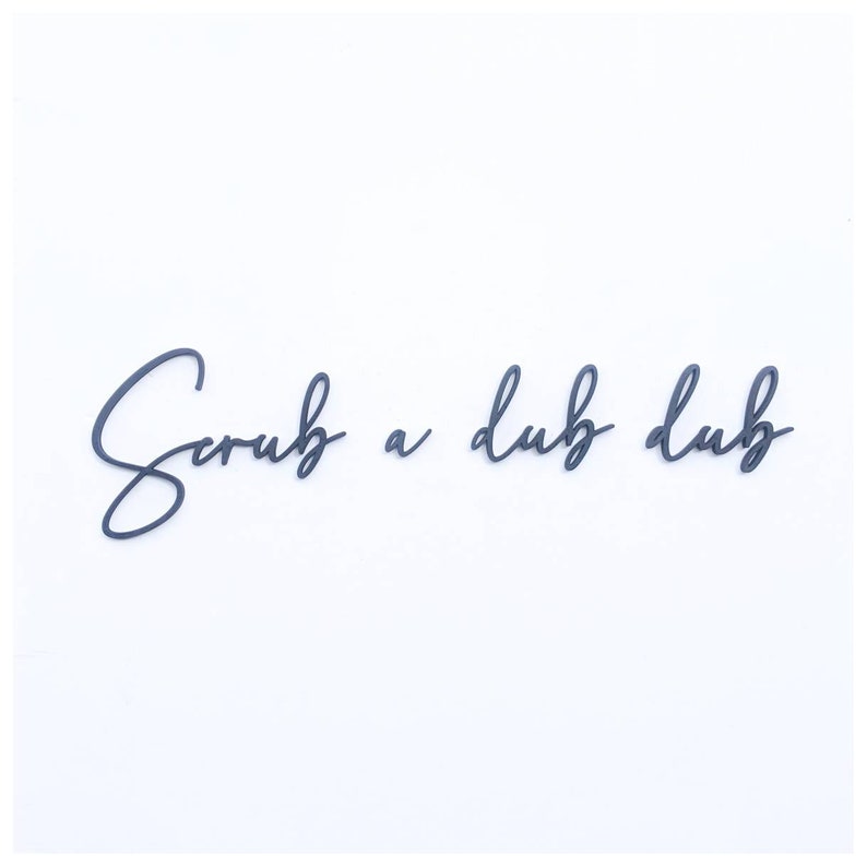 May include: Black cursive script lettering on a white background that reads "Scrub a dub dub".