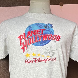 May include: A gray t-shirt with a red and blue graphic of a globe with the text "Planet Hollywood" and "Walt Disney World" printed on it.