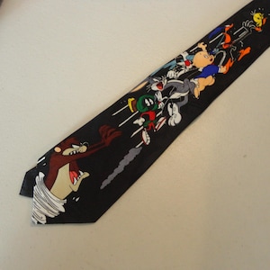May include: Black necktie featuring cartoon characters, including Taz, Bugs Bunny, and others. The tie has a repeating pattern of the characters in motion against a black background. A fun accessory for fans of classic cartoons.