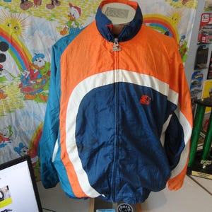 May include: A vintage Starter brand jacket in blue, orange, and white. The jacket has a full zipper, a stand-up collar, and the Starter logo on the chest. The jacket is a retro style and appears to be made of a nylon material.
