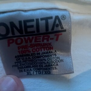 May include: White tag with black text that reads "ONEITA POWER-T PRE-SHRUNK 100% COTTON ASSEMBLED IN JAMAICA OF U.S.A. COMPONENTS PRE-RETRECI/100% COTON PRE-ENCOGIDO/100% ALGODON ENSAMBLADO EN JAMAICA DE E.U.A. COMPONENTES. XL/TG/XG"