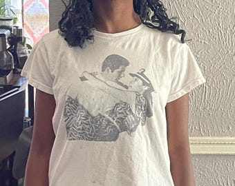 May include: White t-shirt featuring a grayscale graphic of two people embracing. The image on the shirt appears to be a still from a movie or a romantic scene. The shirt has short sleeves and a crew neck.