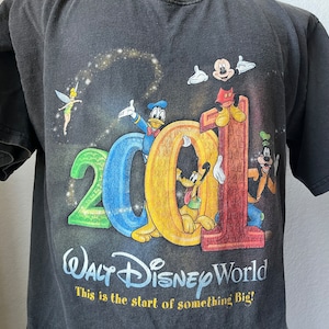 Puede incluir: Camiseta negra con un gr&aacute;fico colorido de Mickey Mouse, Donald Duck, Goofy y Campanilla celebrando el 2001 en Walt Disney World. El texto "This is the start of something Big!" est&aacute; impreso debajo del gr&aacute;fico.