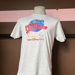 May include: Gray t-shirt with a blue and red graphic that says "Planet Hollywood" with five yellow stars and the text "Walt Disney World" underneath.