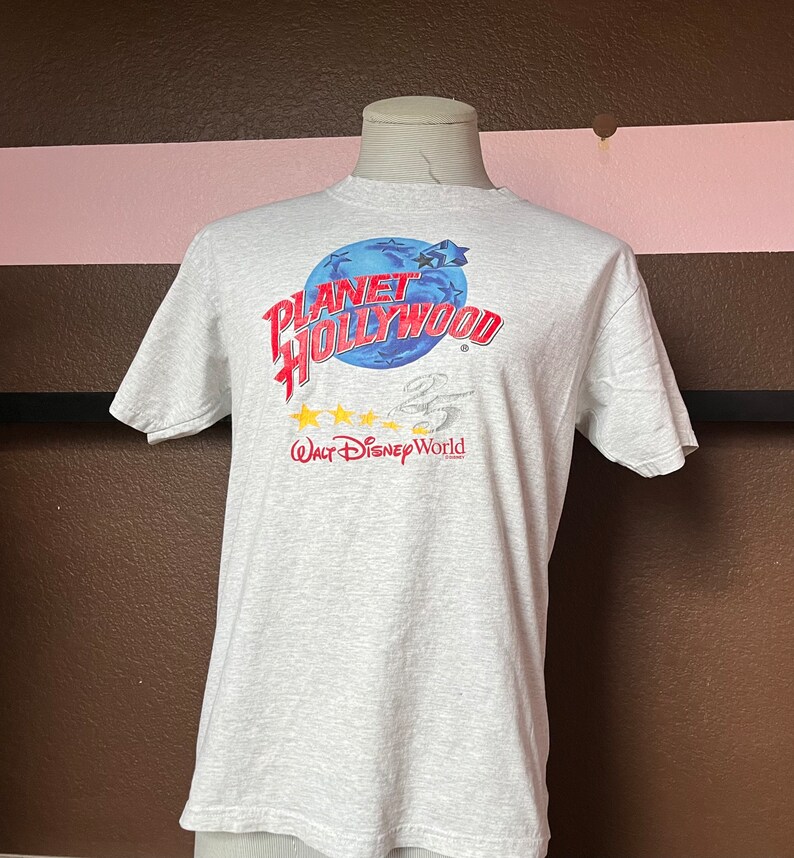 May include: Gray t-shirt with a blue and red graphic that says "Planet Hollywood" with five yellow stars and the text "Walt Disney World" underneath.