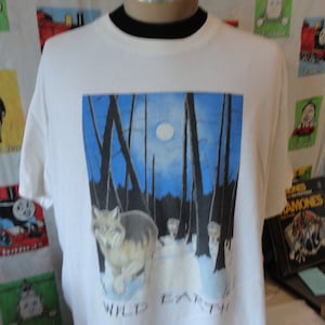 May include: White t-shirt with a graphic of a wolf in a forest under a full moon. The text "Wild Earth" is printed below the image.